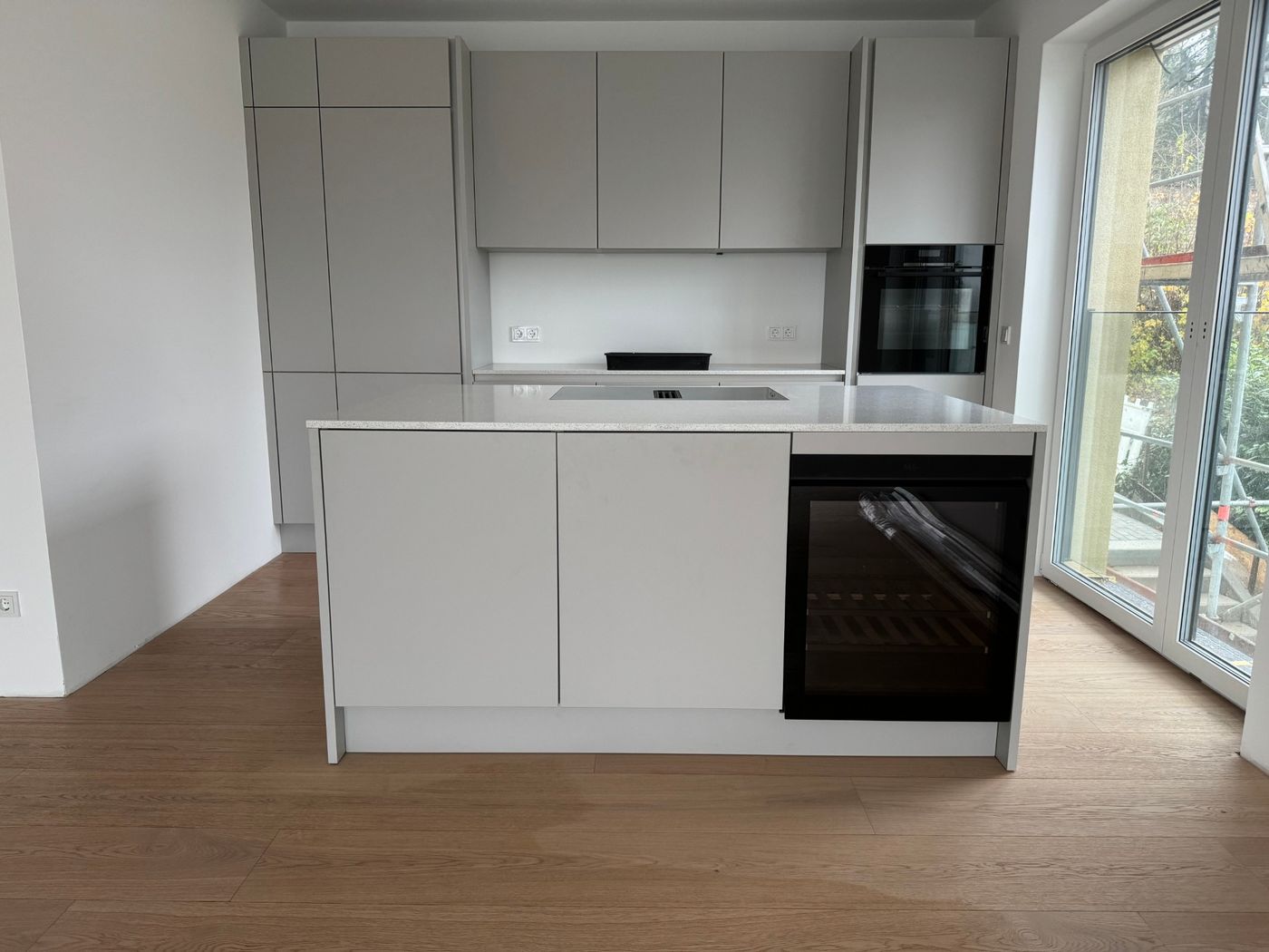 Grifflose helle Küche mit Kochinsel, Weinkühlschrank und Eichenparkett